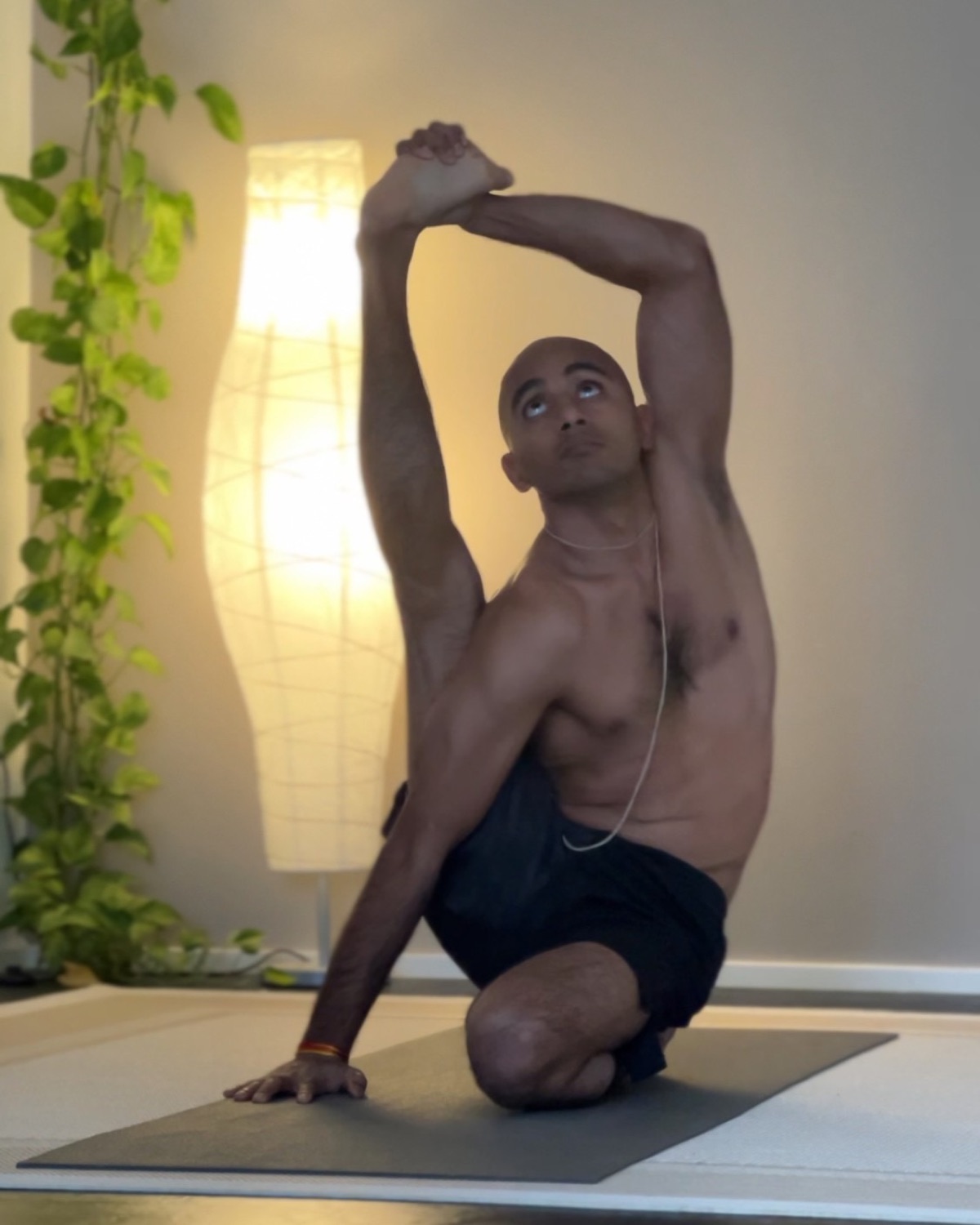 Pratiush Sharma in a seated spinal twist with one leg raised, warm lamp light